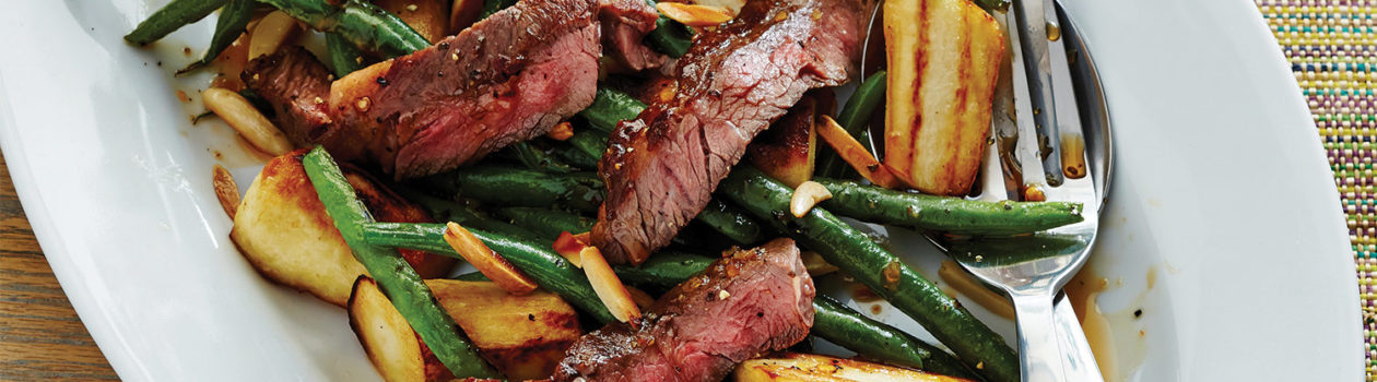 A close-up picture of medium-rare steak chunks served on a bed of pan-seared green beans and crispy parsnip bites.