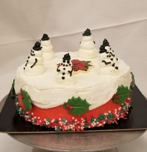 A round cake decorated with red icing, mistletoe and sprinkles and six snowmen on top. 