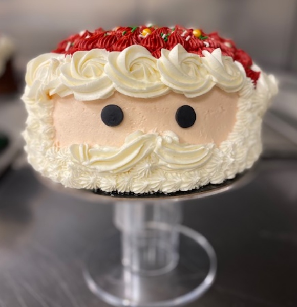 A round cake with a santa decorated on the side and red icing on top as a hat.