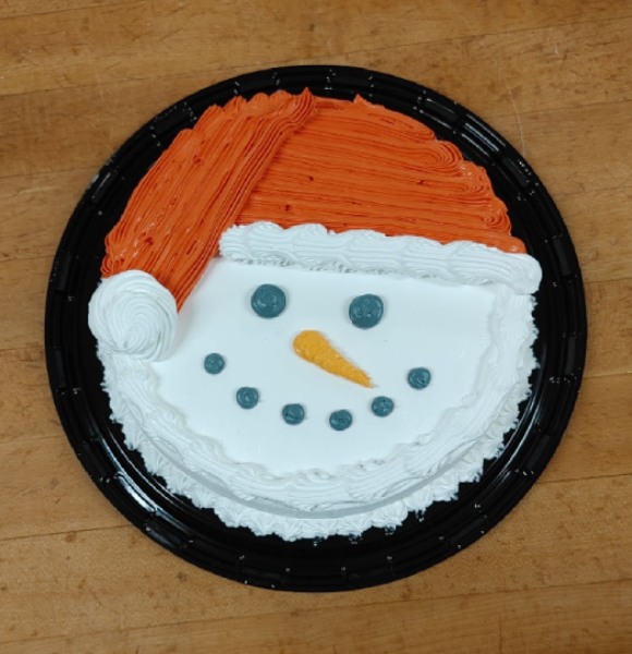 An overhead shot of a round cake with a snowman wearing a red and white santa hat.