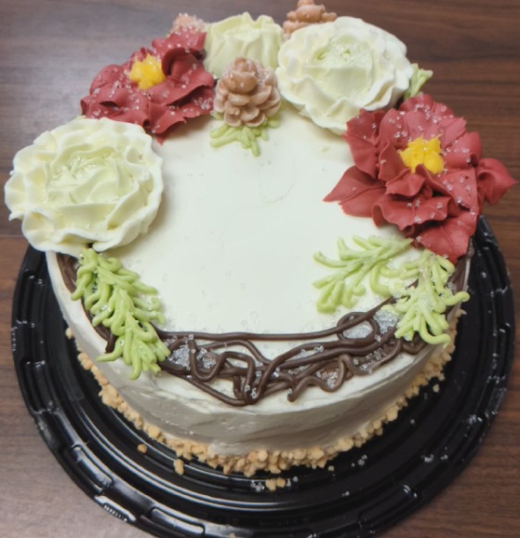 A round white cake decorated with red flowers and pine leaves and fake snow.