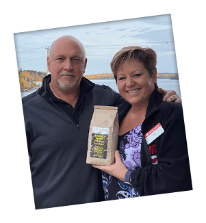 Warren and Cindi Lumgair of Red Lake IGA in front of a local landscpae holding a bag of Flying Wild Rice.