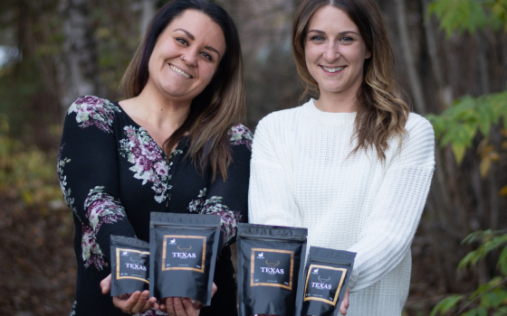 Kate Porobic and Audry Gavin standing outdoors together with trees in background, they are holding packages of spices.
