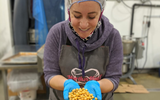 Founder Nada wears hairnet, apron, gloves and is in factory setting with large vat of chickpeas.