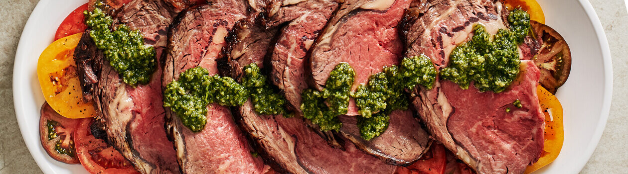 Sliced prime rib roast with pesto drizzled on top