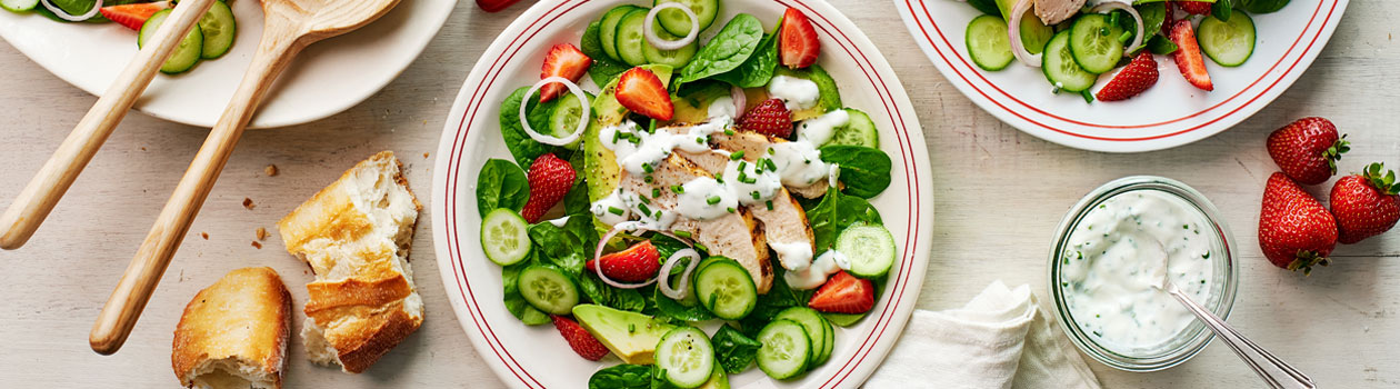 Overhead shot for Strawberry and Chicken Spinach Salad in two plates with dressing and torn baguette on the side.