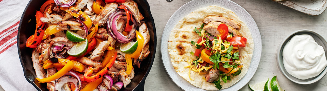 Grill pan with fajita ingredients beside a plate with a finished fajita and bowl of peach salsa