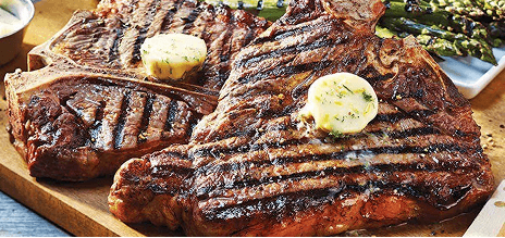 Grilled T-bone steaks topped with herb butter and served with grilled asparagus.